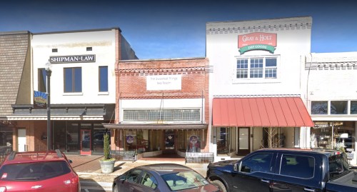 A street view of a small town with shops, including a law office and a dry goods store, parked cars in front.