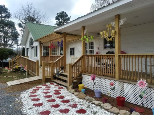 A charming house with a wooden porch, colorful flowers, and decorative elements, set against a cloudy sky.