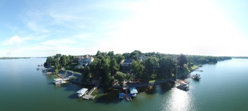 Aerial view of a serene lake surrounded by lush greenery and waterfront homes, with boats docked along the shore.