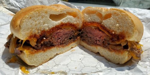 A halved burger with melted cheese, grilled onions, and a juicy beef patty, served in a soft bun.
