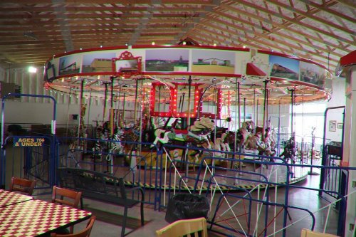 A colorful indoor carousel with various animals, surrounded by tables and decorations in a spacious venue.
