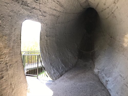 A concrete tunnel with a curved wall, leading to a bright exit and a railing visible in the background.