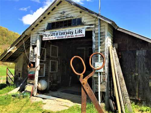 A rustic building labeled "Museum of Everyday Life," featuring large scissors in front and various artifacts displayed.