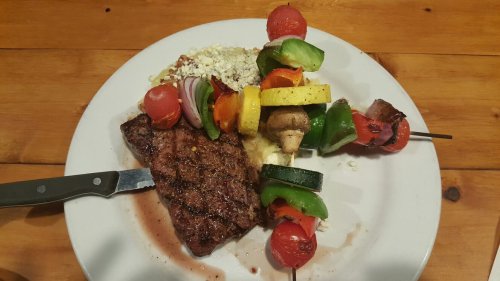 A plate with grilled steak, vegetable skewers, and a side of mashed potatoes, garnished with herbs.