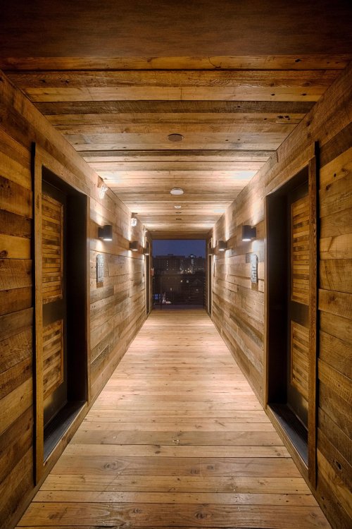 A wooden hallway with lit doors on either side, leading to a view of the city in the distance.