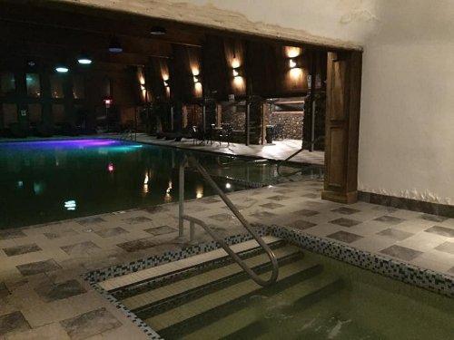 Indoor swimming pool area with dim lighting, featuring a hot tub and lounge chairs.
