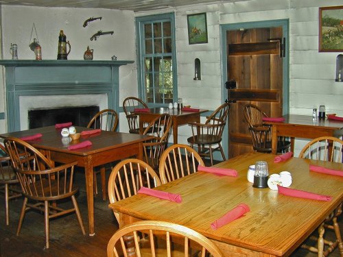 Cozy dining area with wooden tables, chairs, and pink napkins, featuring a fireplace and rustic decor.