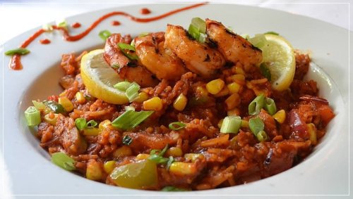 A plate of flavorful shrimp rice with corn, green onions, and lime wedges, garnished with a drizzle of sauce.
