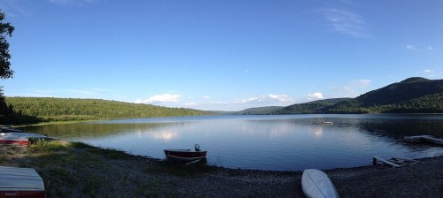 A serene lake surrounded by green hills under a clear blue sky, with boats along the shore.