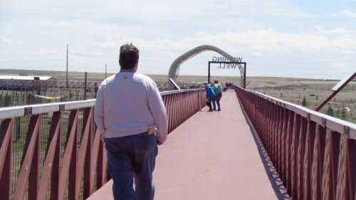 A person walks on a bridge with a sign reading "Waling Well" in the background, surrounded by open landscape.