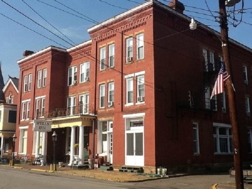 A red brick building with multiple windows, featuring a sign that reads "Wells Inn" and an American flag.