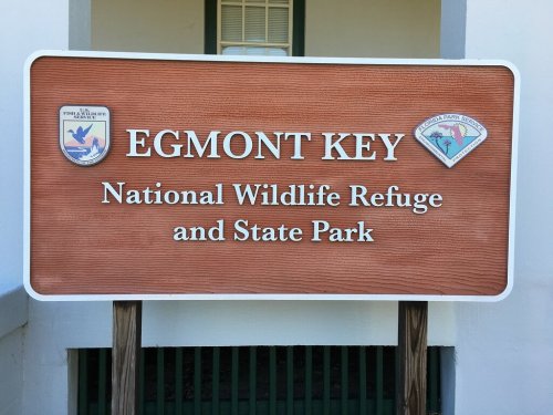 Sign for Egmont Key National Wildlife Refuge and State Park, featuring official logos and a wooden background.