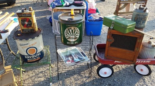 A collection of vintage oil cans, a green toolbox, and a wooden crate displayed at an outdoor market.