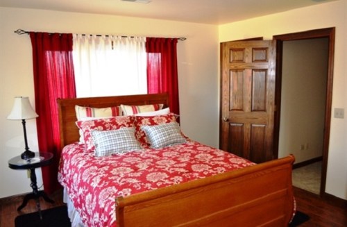 Cozy bedroom featuring a wooden bed with red floral bedding, a nightstand, and a door leading to another room.