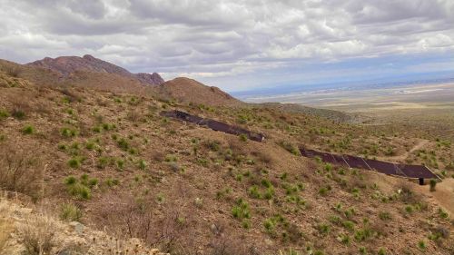 A rugged hillside with sparse vegetation and a winding path leading through the landscape under a cloudy sky.