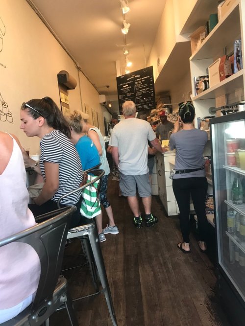 A busy café interior with customers at the counter and seated at tables, featuring a menu board on the wall.