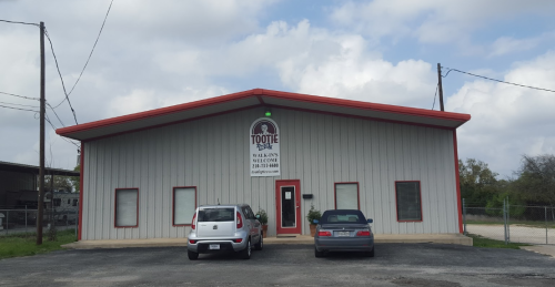 A metal building with a sign reading "Tootie's" and two parked cars in front, under a cloudy sky.