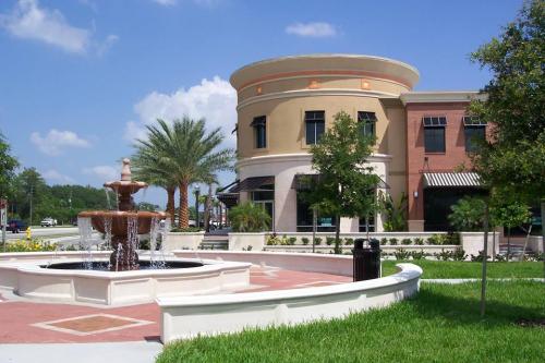 A modern building with a fountain in front, surrounded by palm trees and green grass under a blue sky.