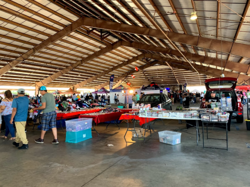A bustling indoor market with vendors selling various items under a large, open structure.