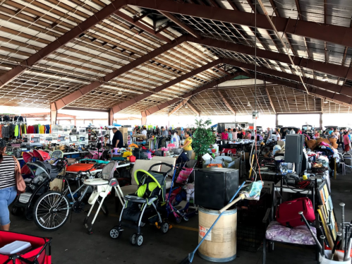A bustling indoor market filled with various items for sale, including furniture, clothing, and strollers.