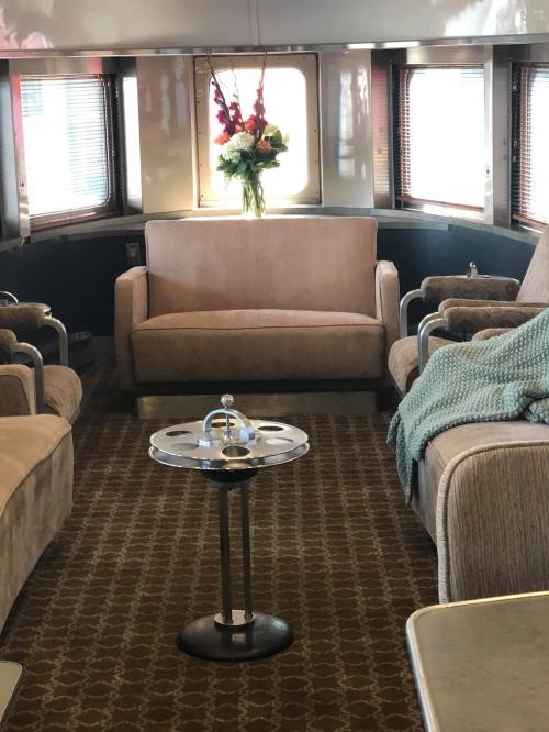 Cozy interior of a train car featuring a sofa, armchairs, a small table, and a floral arrangement.