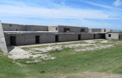 A weathered concrete structure with multiple doorways, set against a blue sky and grassy foreground.