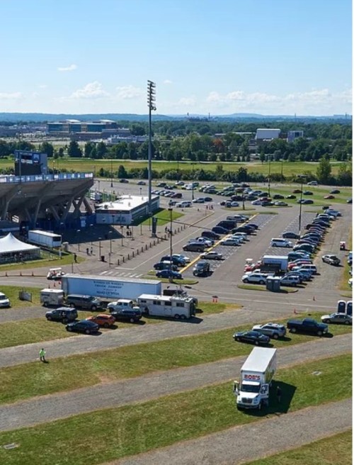 Aerial view of a parking lot with cars and trucks, near a stadium on a sunny day with clear skies.