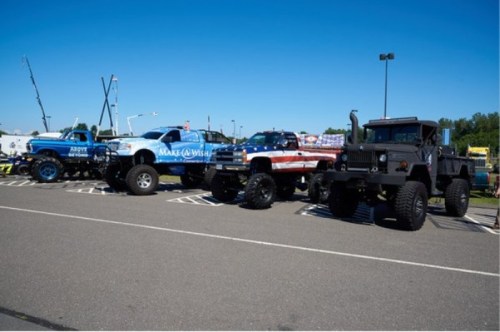 A lineup of four customized trucks parked in a lot, showcasing vibrant designs and unique modifications under a clear blue sky.