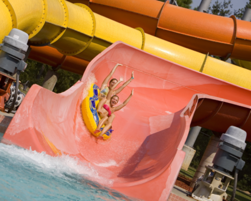 Two children joyfully slide down a colorful water slide, splashing into the pool below.