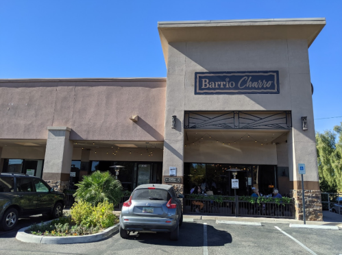 Exterior of Barrio Charro restaurant with a clear blue sky, featuring outdoor seating and parked cars in front.