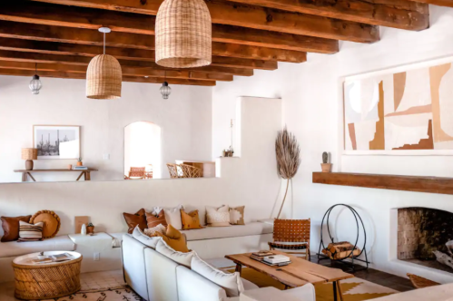 A cozy living room with white walls, wooden beams, and stylish decor, featuring a sofa, coffee table, and woven accents.