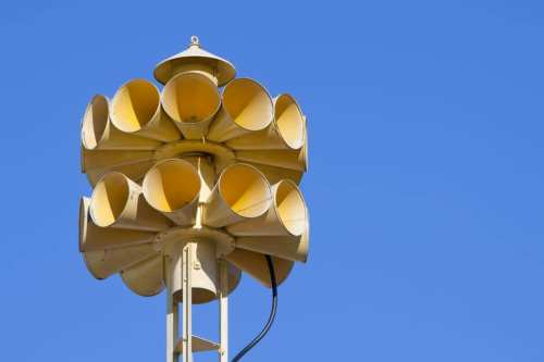 A tall structure topped with multiple yellow horns against a clear blue sky.