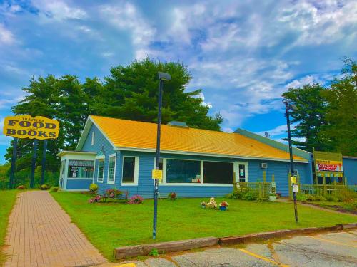 A blue building with a yellow roof, featuring signs for "Traveler's Food" and "Books," surrounded by greenery and flowers.