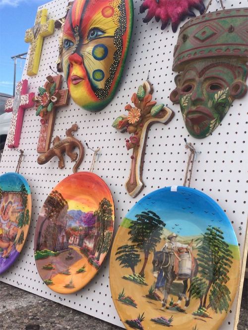 Colorful masks and decorative plates displayed on a pegboard, featuring intricate designs and vibrant colors.