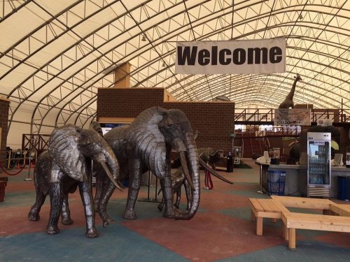 Three elephant sculptures inside a large tent, with a "Welcome" banner overhead and a seating area in the background.