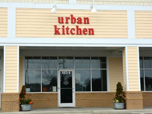 Exterior of a restaurant named "urban kitchen," featuring a glass door and decorative plants at the entrance.