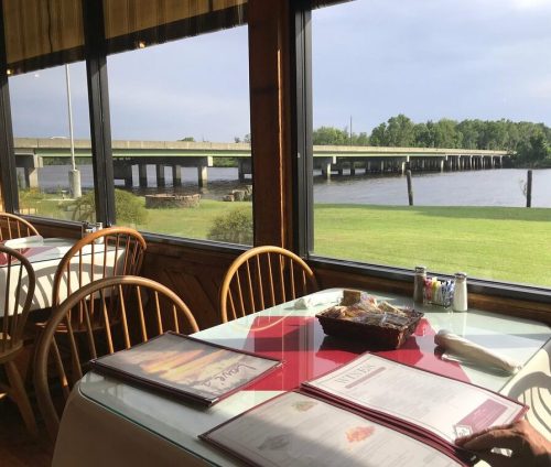 A riverside restaurant with a view of a bridge, featuring tables set for dining and a menu on the table.