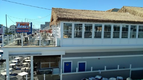 A beach bar with a thatched roof and outdoor seating, overlooking a sunny coastal area.