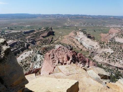 A panoramic view of rugged, colorful rock formations and a vast landscape under a clear blue sky.