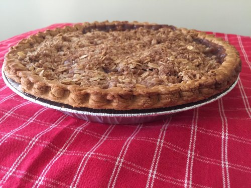 A freshly baked pie with a crumbly topping on a red checkered tablecloth.
