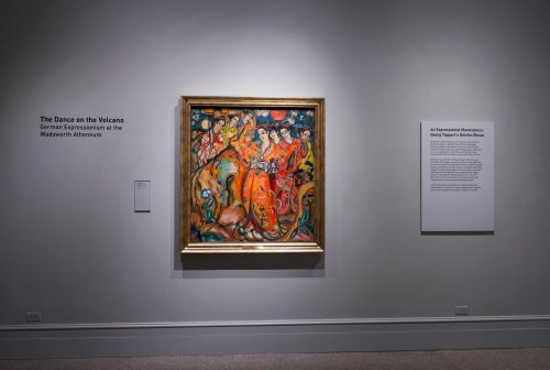 A vibrant painting titled "The Dance on the Volcano" displayed in a gallery, with informational text on the wall.