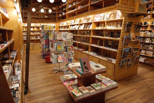 A cozy bookstore interior with wooden shelves filled with books and magazines, illuminated by warm lighting.