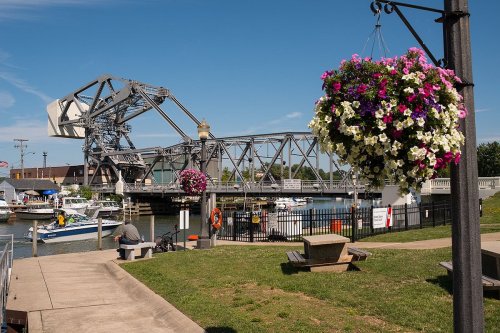 A scenic view of a bridge with flowers hanging nearby, overlooking a marina with boats and a clear blue sky.