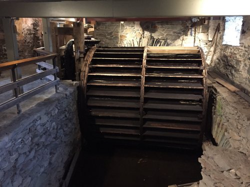 A large wooden water wheel inside a stone building, partially submerged in water, with rustic surroundings.