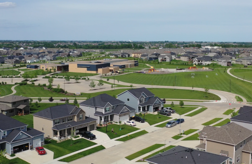 Aerial view of a suburban neighborhood with houses, green spaces, and a school in the background.