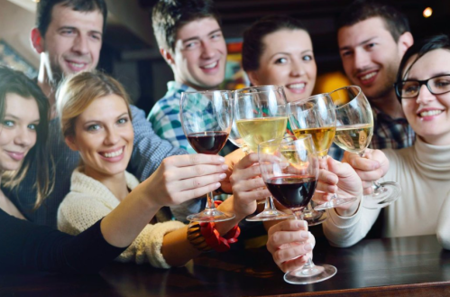 A group of smiling friends toasting with various drinks in a lively setting.