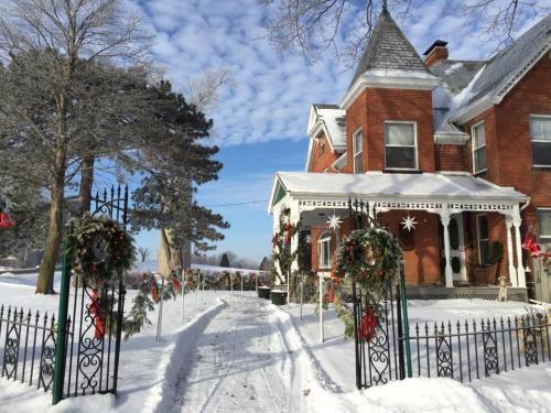 A snowy scene featuring a brick house with festive decorations and a path lined with wreaths and trees.
