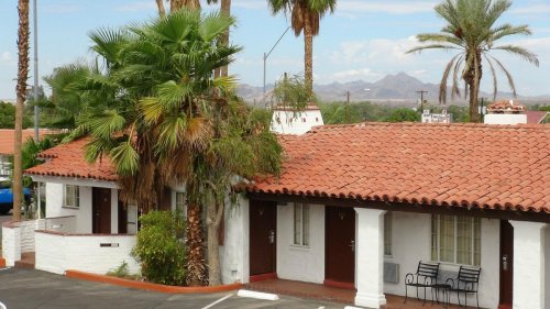 A view of a southwestern-style building with palm trees and mountains in the background under a clear blue sky.