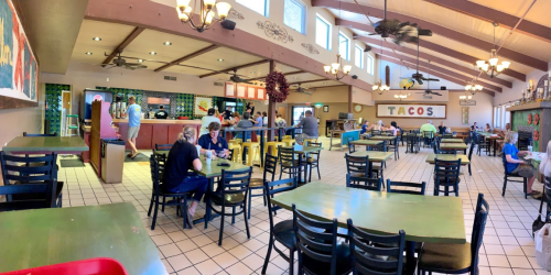 A spacious taco restaurant with colorful decor, tables filled with diners, and a counter in the background.