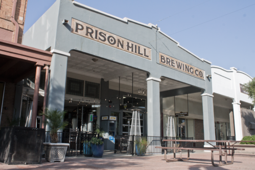 Exterior of Prison Hill Brewing Co., featuring a large sign and outdoor seating area.